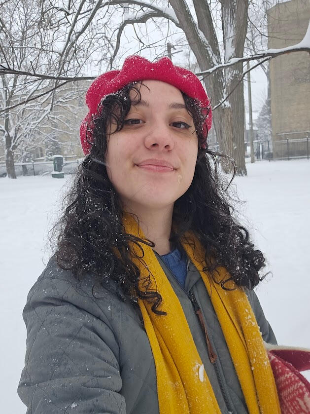Monica headshot A photo of me, Monica! I'm a young light-skinned Latina woman with curly brown hair wearing a patchwork denim vest. I'm standing in front of foliage and laughing.